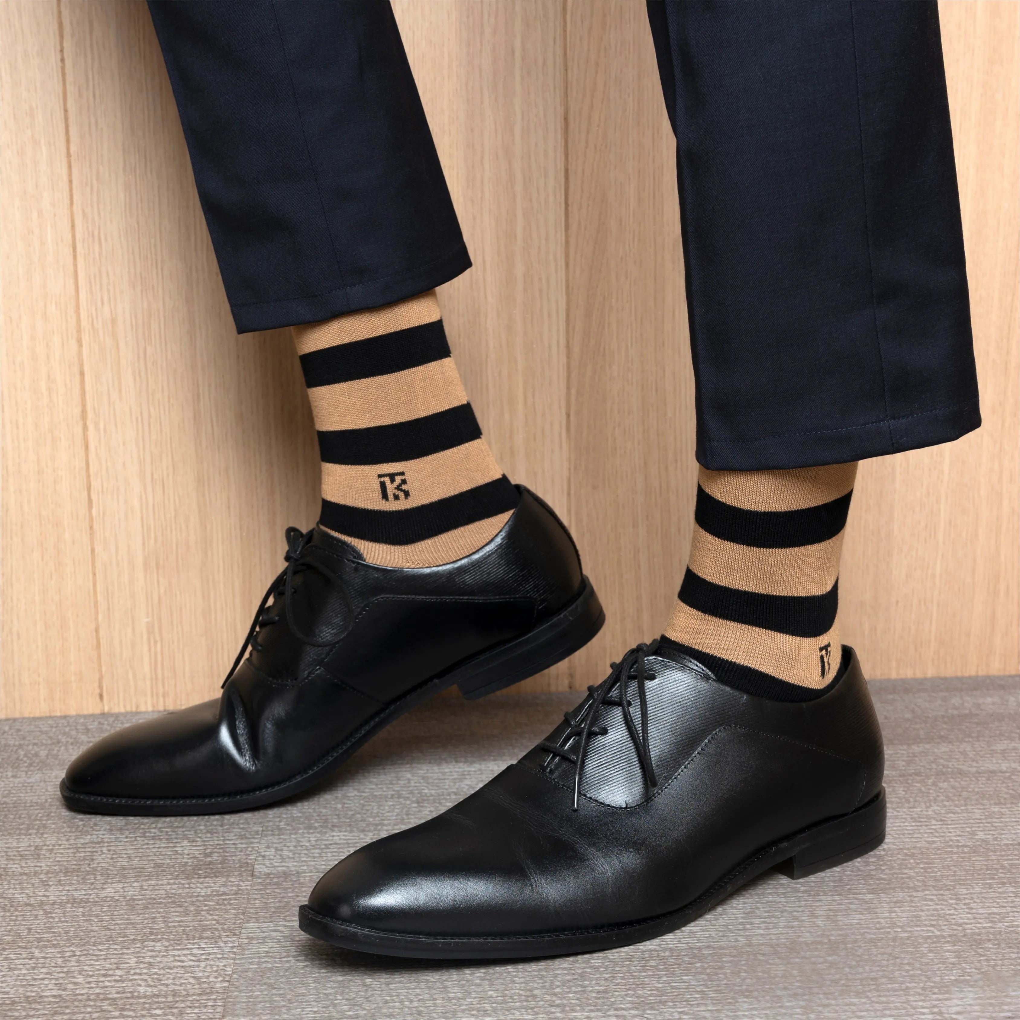 Men's tan and black striped bamboo socks worn with professional black oxford shoes and navy slacks.